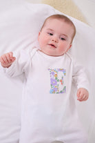 a happy baby wearing a cotton baby romper with her initial on the front in betsy purple floral liberty print. 