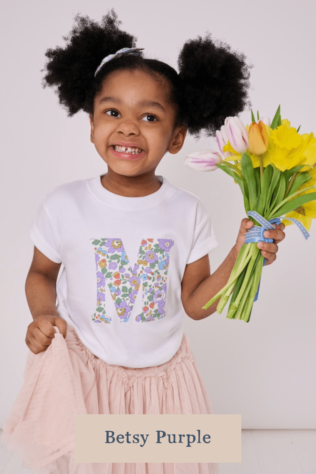 A 3 year old girl wearing a personalised white cotton t-shirt with her initial on in Betsy Purple floral Liberty fabric.