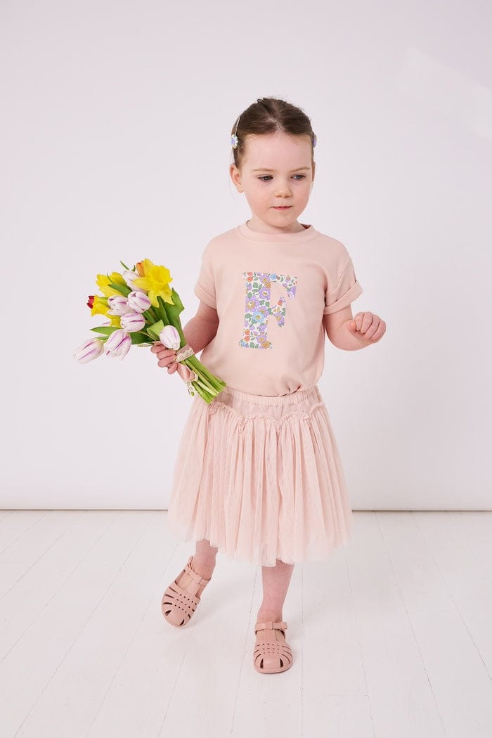 a 4 year old girl wearing a personalised kids pink t-shirt with an initial cut from betsy purple liberty floral print on the front
