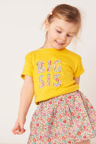 Child wearing a yellow 'BIG SIS' t-shirt with a floral skirt on a white background