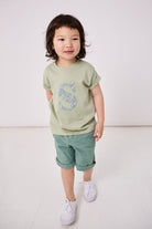 a 4 year old boy wearing a personalised kids sage green t-shirt with an initial cut from brave noah dragons liberty print on the front.