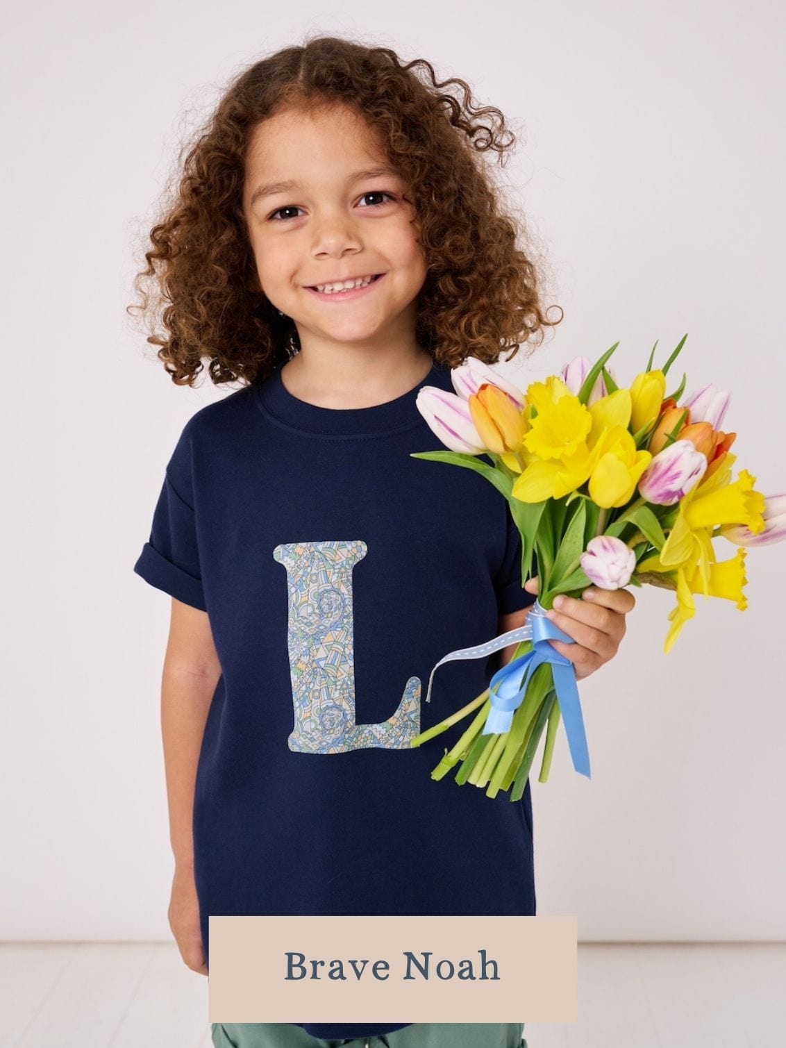 a 5 year old boy wearing a personalised kids navy t-shirt with an initial cut from brave noah liberty print on the front.