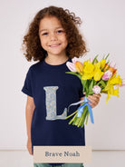 a 5 year old boy wearing a personalised kids navy t-shirt with an initial cut from brave noah liberty print on the front.