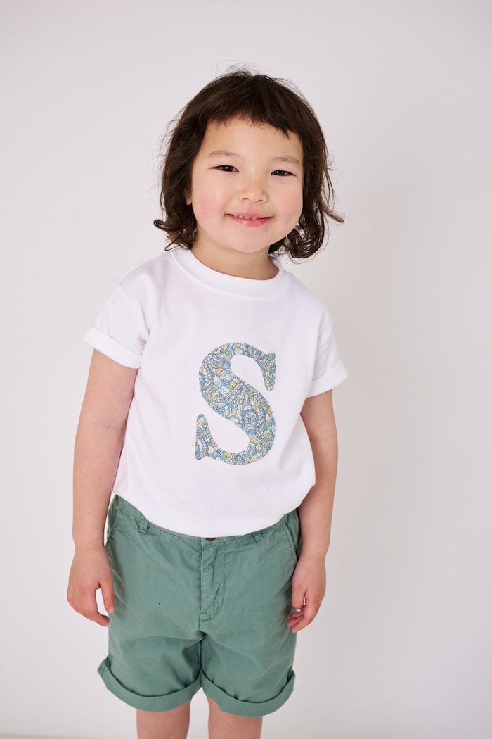 a 4 year old boy wearing a personalised kids white t-shirt with an initial cut from brave noah dragons liberty print on the front
