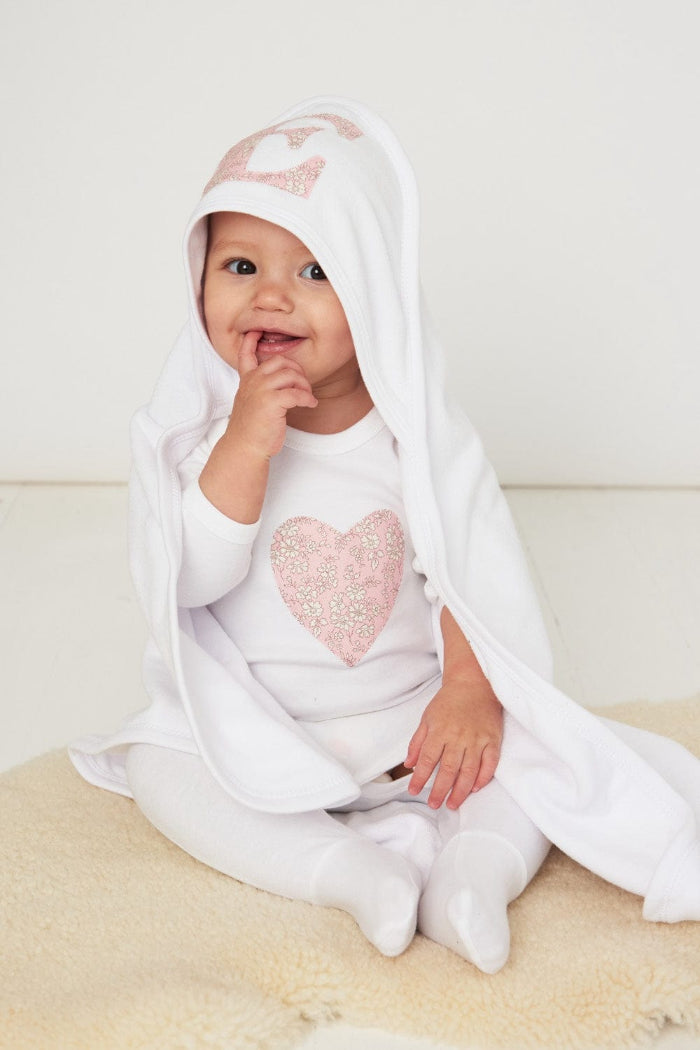 a happy baby wearing a cotton baby romper with a heart on the front in capel pink floral liberty print. 
