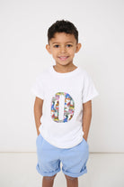 A smiling 4 year old  wearing a white kids T-Shirt with his initial on the front in Dinosaur Liberty Print