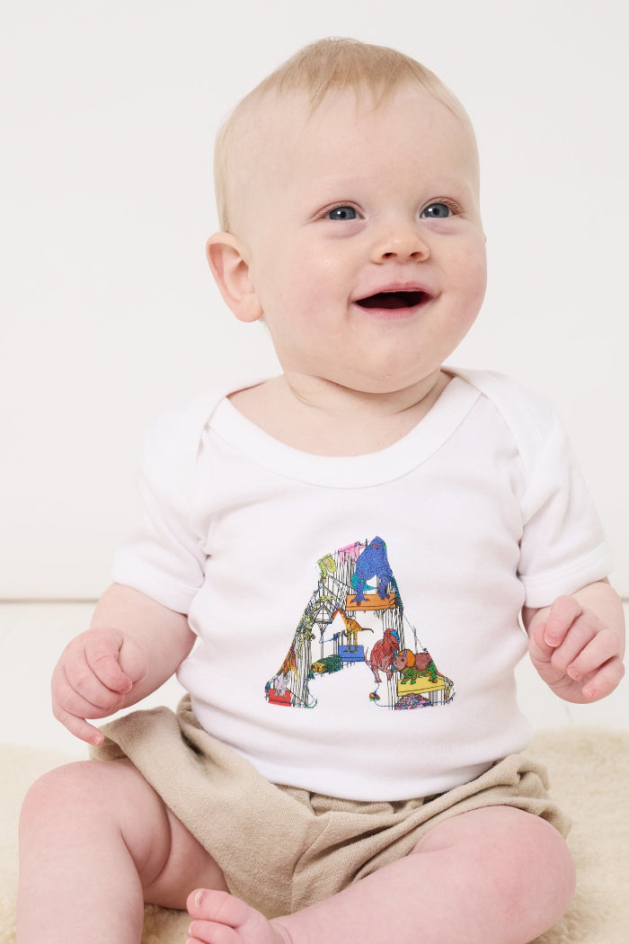 A baby wearing a personalised baby bodysuit with his initial cut from dinosaur liberty print on the front