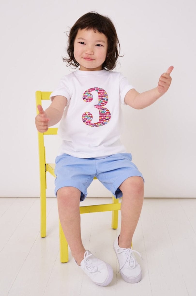 a 3 year old  boy is wearing a personalised kids white t-shirt with a number 3 cut from Hop on hop off red cars and london bus liberty print on the front