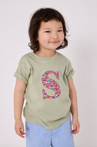 a 4 year old boy wearing a personalised kids sage green t-shirt with an initial cut from hop on hop off res london bus and cars liberty print on the front.