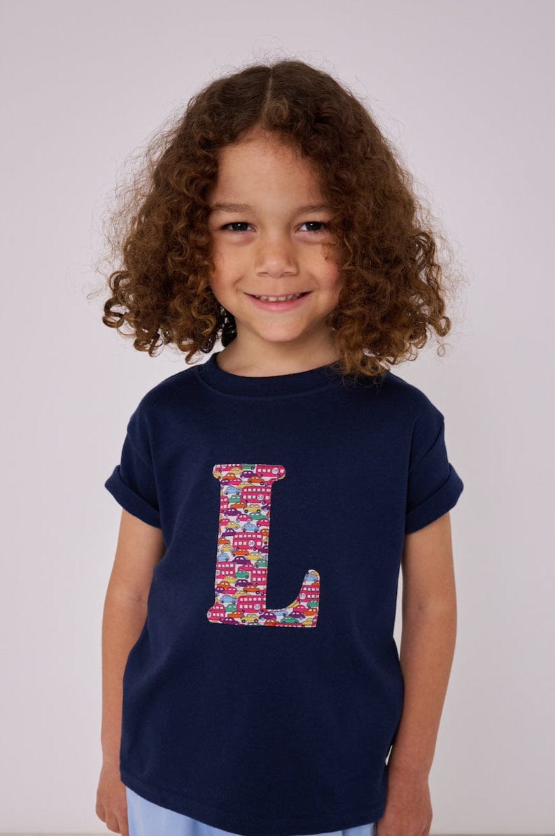 A child wearing a navy t-shirt with the letter 'L' personalised in a red Hop on hop off Liberty print.