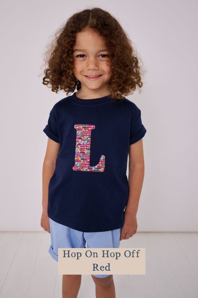 a 5 year old boy wearing a personalised kids navy t-shirt with an initial cut from hop on hop off liberty print featuring london buses and vintage cars
