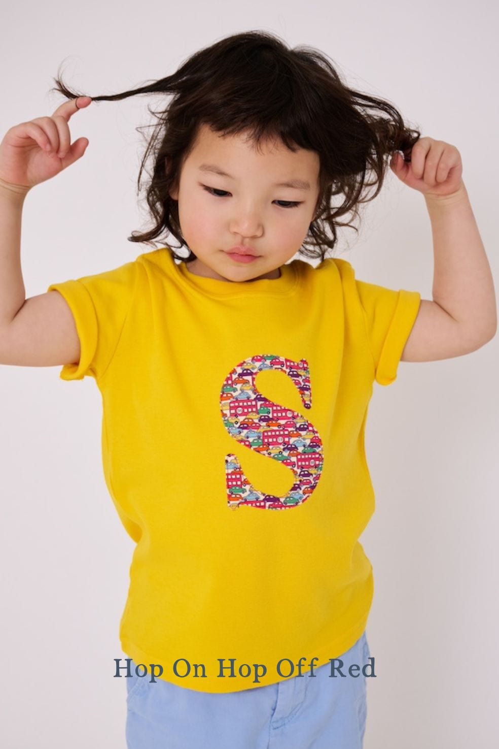 a 3 year old boy wearing a personalised kids yellow t-shirt with an initial cut from hop on hop off red liberty cars and buses print on the front