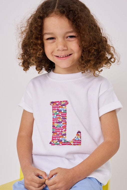a 4 year old  boy is wearing a personalised kids white t-shirt with an initial cut from Hop on hop off red cars and london bus liberty print on the front
