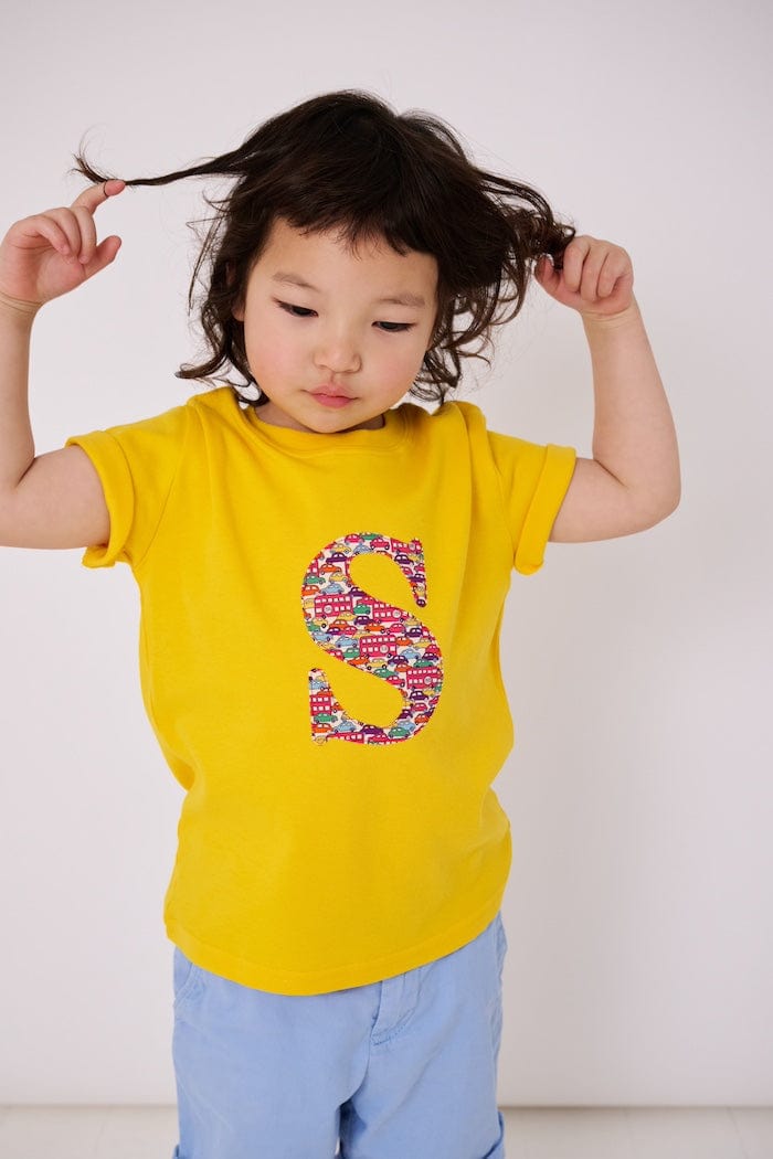 a 4 year old boy is wearing a personalised kids yellow t-shirt with an initial cut from Hop On Hop Off Red Liberty Print on the front 