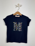 Navy blue t-shirt with colorful Liberty print 'M' design on a wooden hanger against a white background