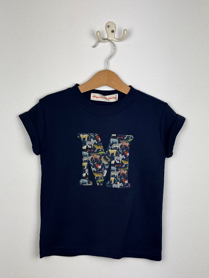 Navy blue t-shirt with colorful Liberty print 'M' design on a wooden hanger against a white background