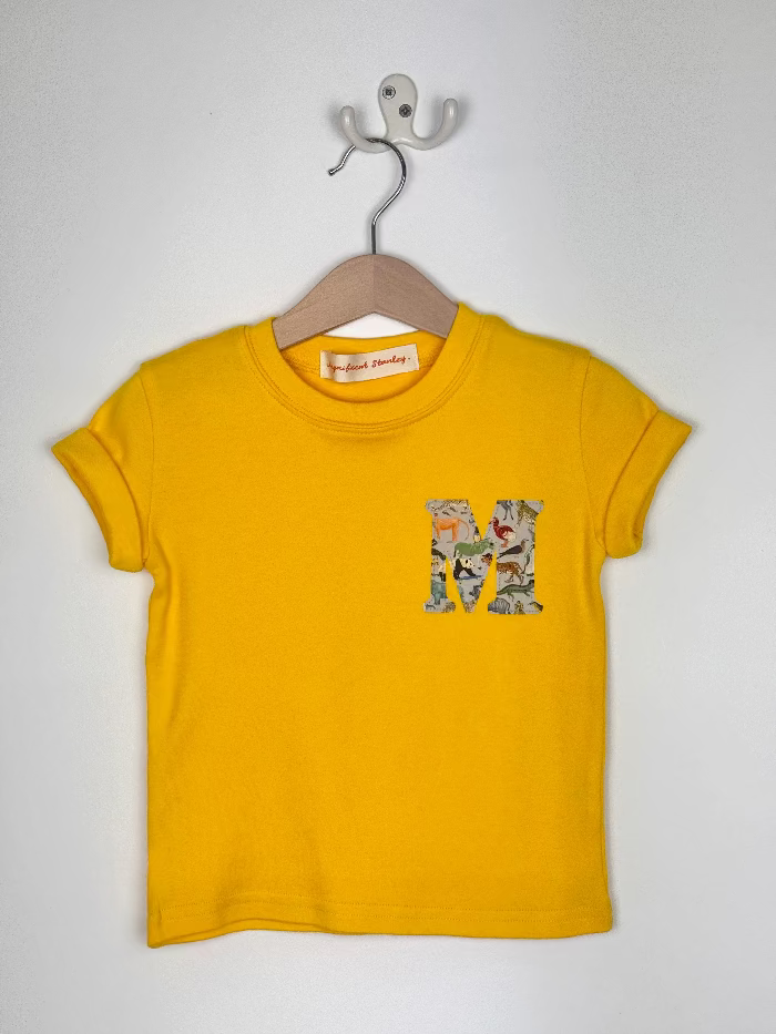 Yellow t-shirt with a liberty zoo print 'M' design on a hanger against a white background