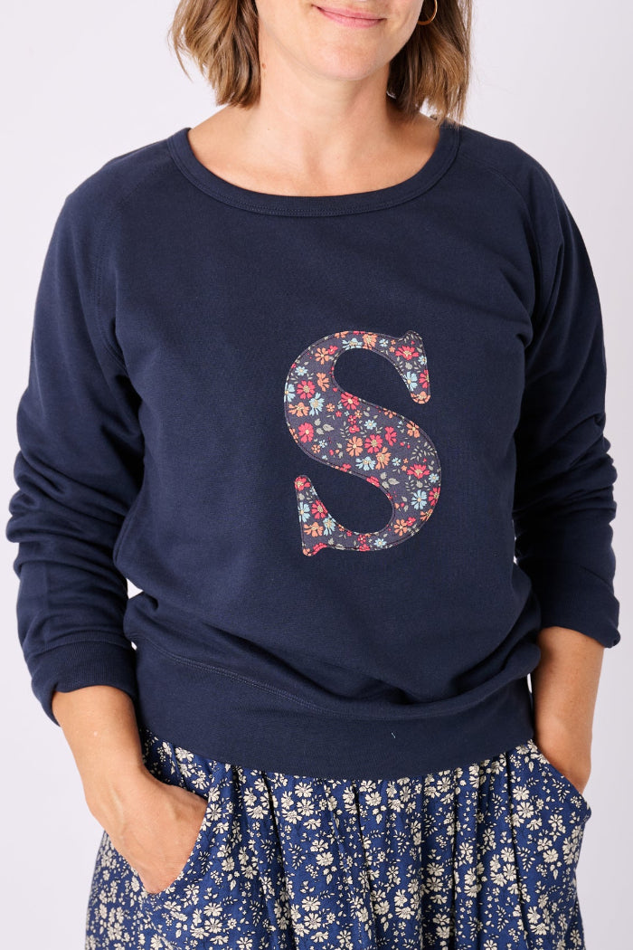 A woman wearing a navy personalised sweatshirt with her initial cut from liberty print on the front.