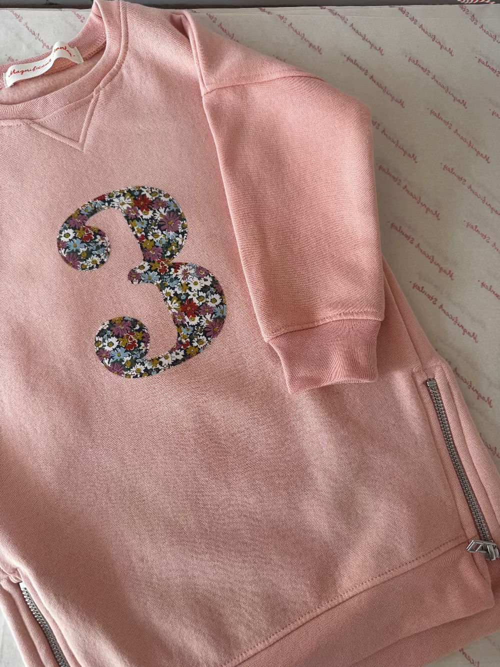 A pink girl's sweatshirt dress with a liberty print number 3 on the front.