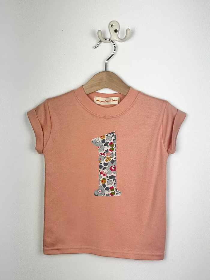 Pink t-shirt with a floral number one design on a hanger against a white background