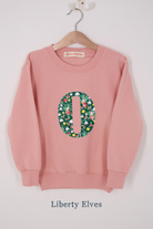 A pink personalised sweatshirt with an initial sewn on to the front. The initial is made from liberty elves print