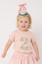 A birthday girl wearing a pale pink t-shirt with a Liberty Nazanin floral number '2' on the front.
