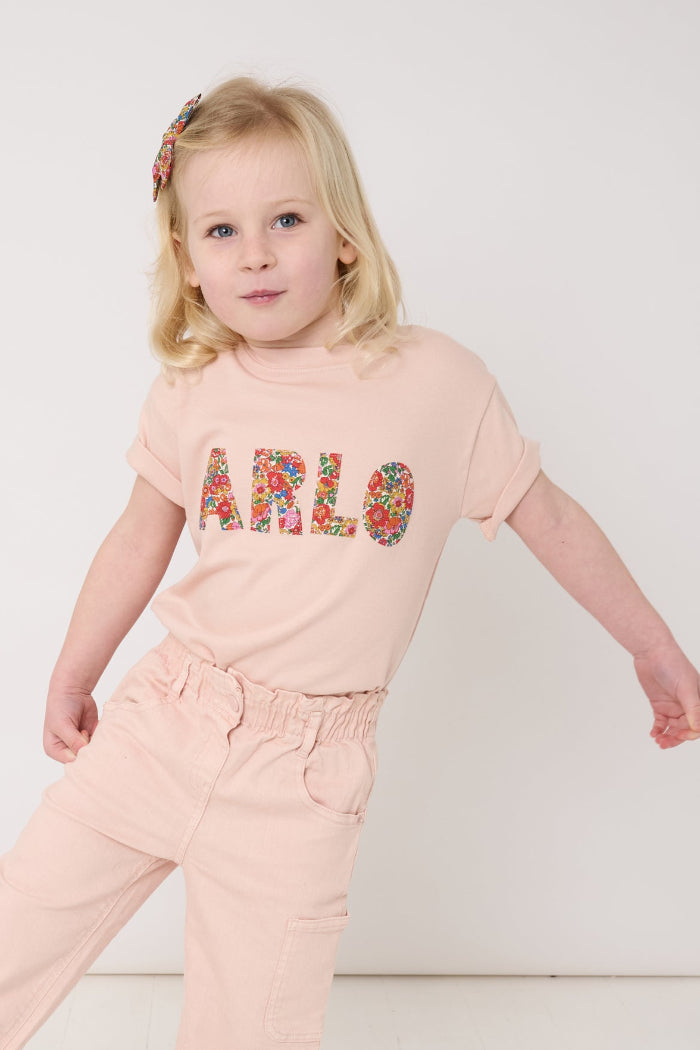 A young girl wearing a pink t-shirt with her name on the front in Liberty Nell Annie May floral print.