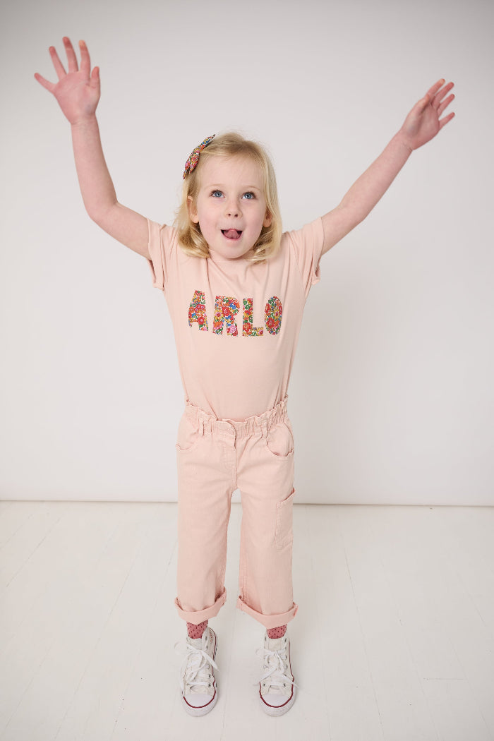 A young girl wearing a pink t-shirt with her name on the front in Liberty Nell Annie May floral print.