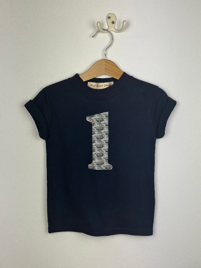 Navy blue t-shirt with a liberty ship patterned number '1' on a hanger against a white background