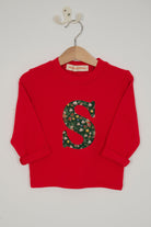 A festive children's outfit set featuring a bright red long-sleeve top with a large green floral monogram letter 'S' on the chest made from Liberty Elves print.