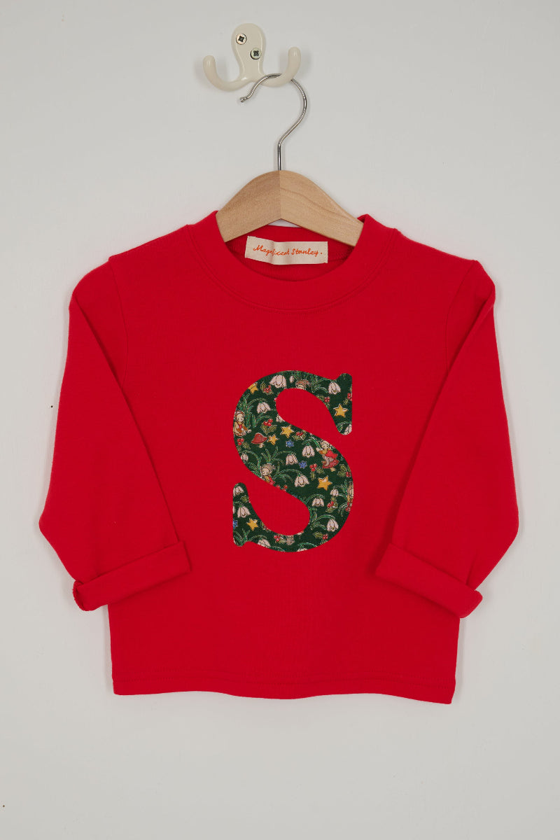 A festive children's outfit set featuring a bright red long-sleeve top with a large green floral monogram letter 'S' on the chest made from Liberty Elves print.