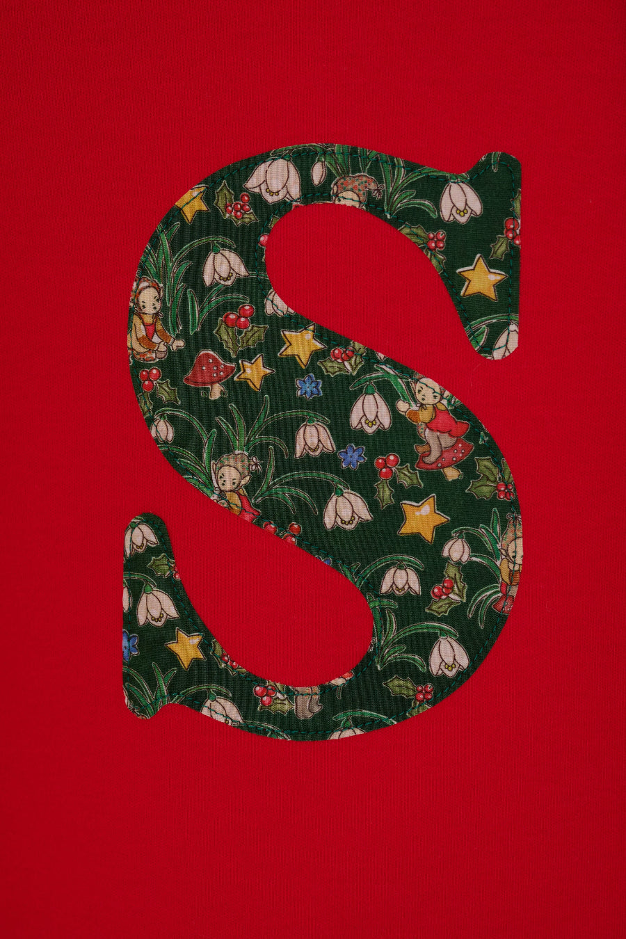 A festive children's outfit set featuring a bright red long-sleeve top with a large green floral monogram letter 'S' on the chest made from Liberty Elves print.