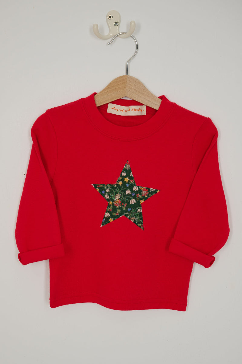 A red long-sleeve sweatshirt with a large star-shaped patch on the chest featuring a Christmas Liberty Elves print.