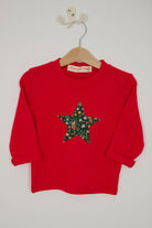 A red long-sleeve sweatshirt with a large star-shaped patch on the chest featuring a Christmas Liberty Elves print.
