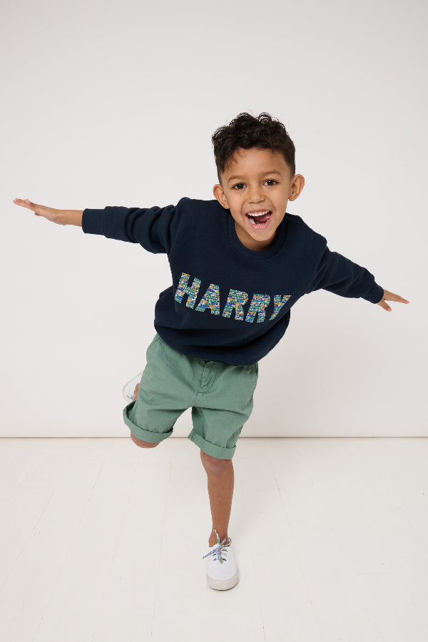 Child wearing a navy sweatshirt with his name 'HARRY' sewn on it, standing against a white background