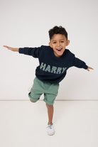 Child wearing a navy sweatshirt with his name 'HARRY' sewn on it, standing against a white background