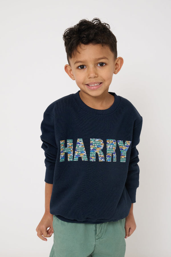 Child wearing a personalised navy blue sweatshirt with 'HARRY' printed in colourful letters on a white background