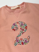 Pink sweatshirt with a liberty floral number '2' on a white background