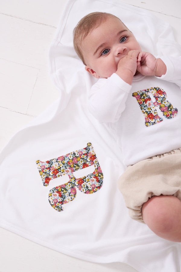 A newborn baby laying on Personalised Liberty Print Cotton Baby Blanket with their initial sewn on it.