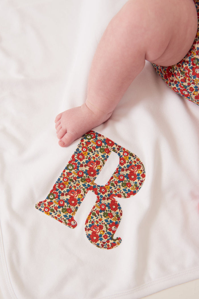 A newborn baby laying on Personalised Liberty Print Cotton Baby Blanket with their initial sewn on it.