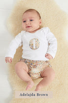 A smiling newborn baby wearing a personalised white bodysuit with an initial on the front cut from Liberty Adelajda starry fabric.