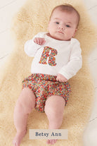 A smiling newborn baby wearing a personalised white bodysuit with an initial on the front cut from Liberty floral fabric.