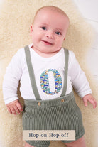 A smiling newborn baby wearing a personalised white bodysuit with an initial on the front cut from Liberty cars fabric.