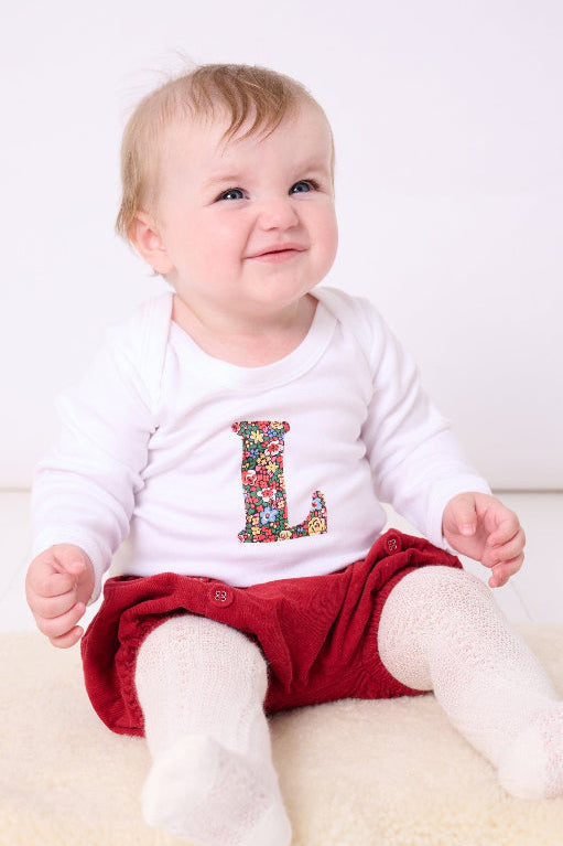 A baby wearing a personalised baby grow with her initial on cut from Liberty Emma Louise cotton fabric.