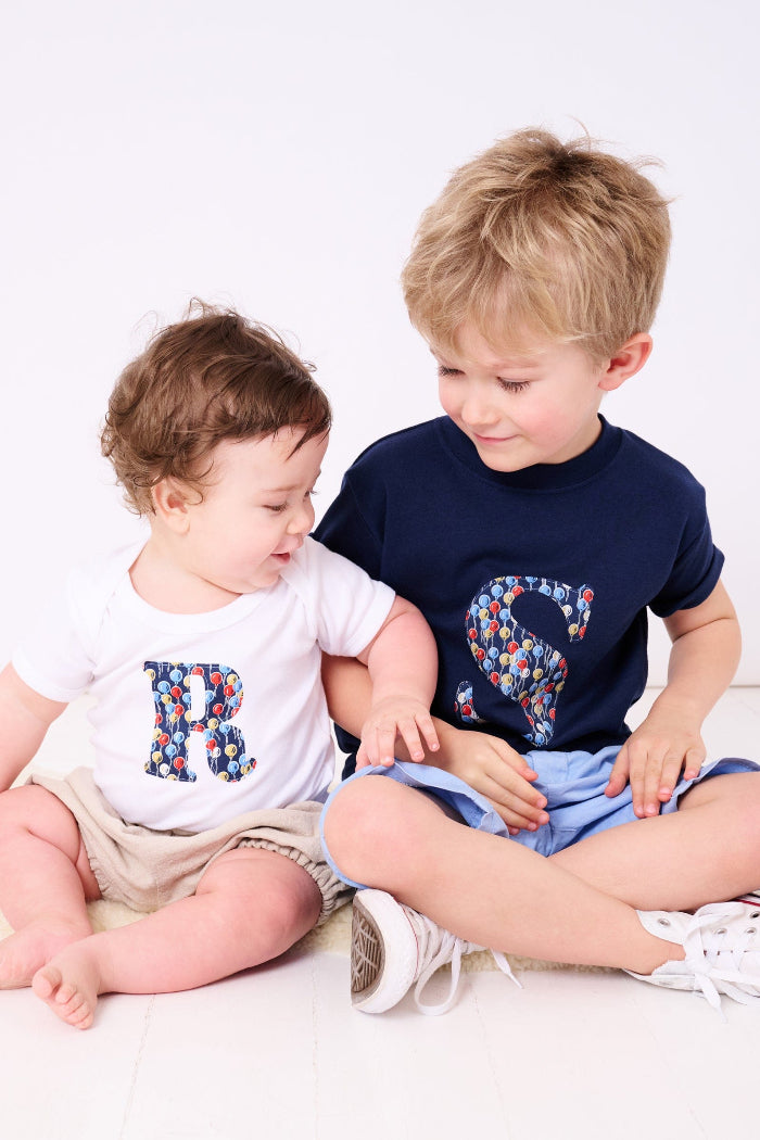 A baby wearing a Personalised Bodysuit in Ethan's Party Liberty Print with his brother wearing a matching personalised kids t-shirt