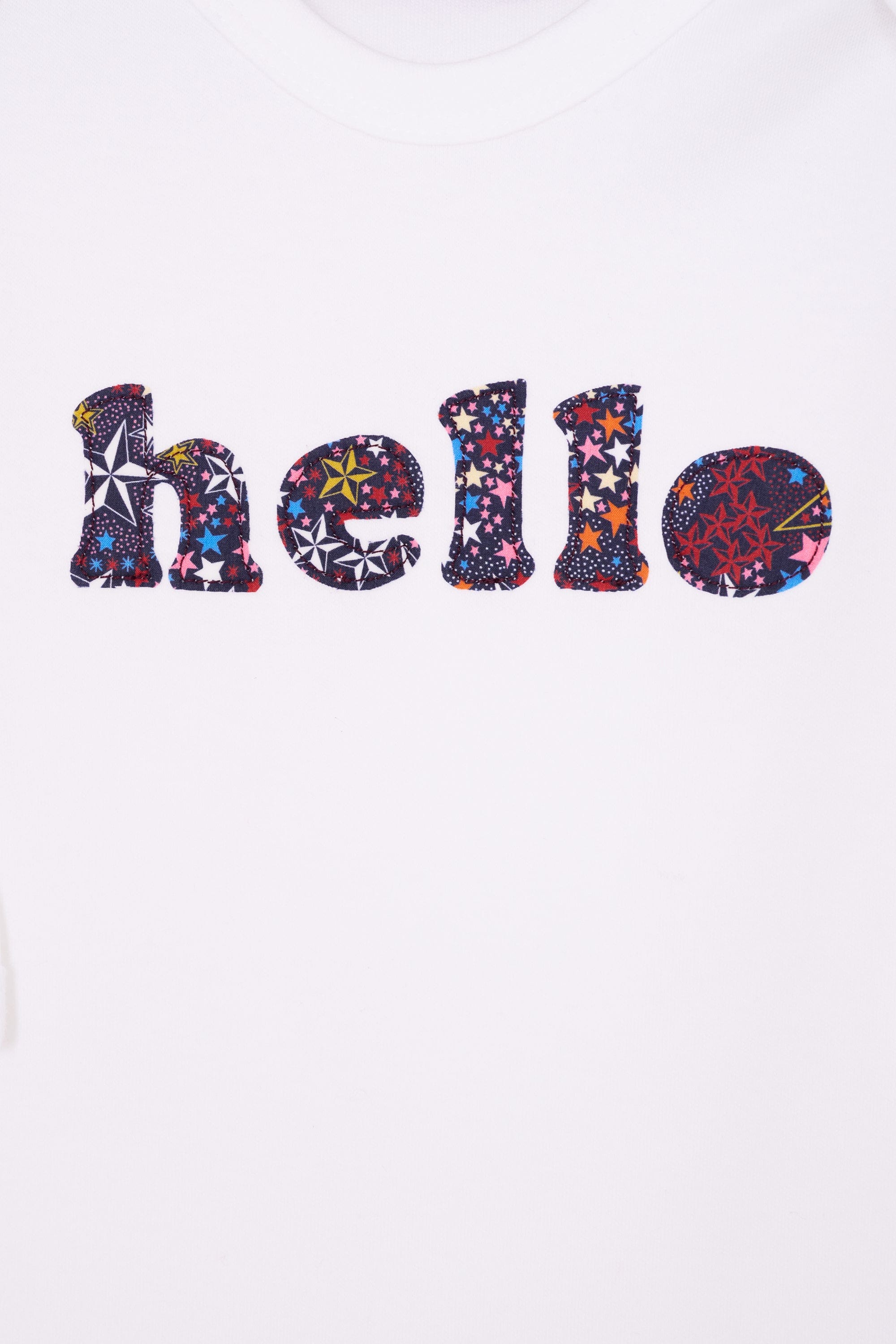 Close up of a white cotton romper with the word hello on it. the letters are cut from starry liberty print and appliquéd onto the romper