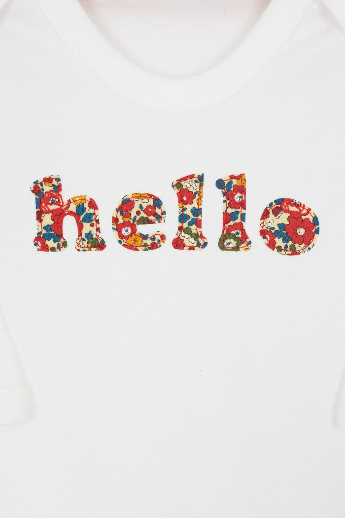 Close up of a white cotton romper with the word hello on it. the letters are cut from floral liberty print and appliquéd onto the romper