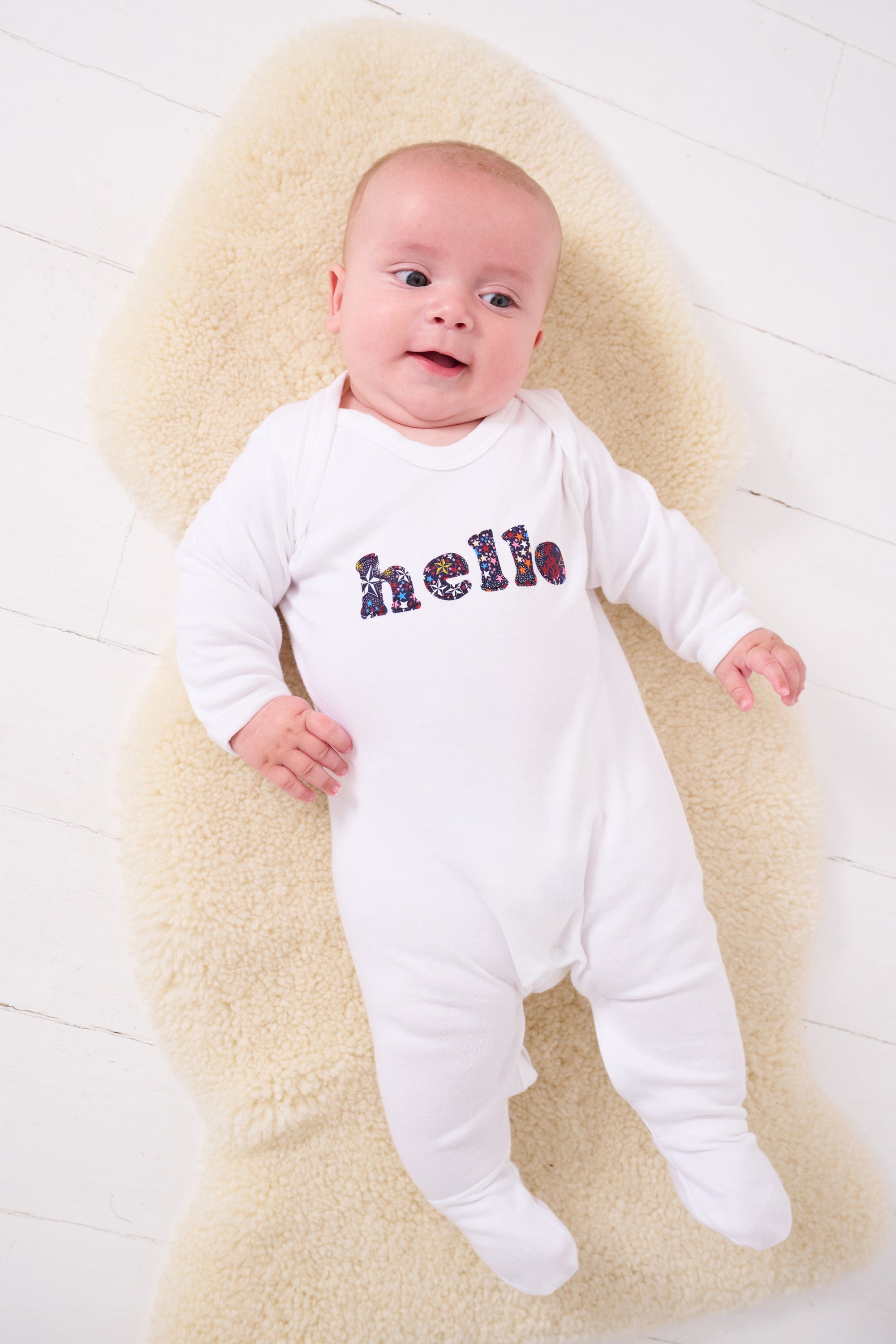 A new baby wears a white cotton romper with the word hello on it. the letters are cut from starry liberty print 