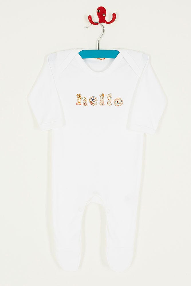 Close up of a white cotton romper with the word hello on it for a new baby. the letters are cut from adelajda star liberty print and appliquéd onto the romper