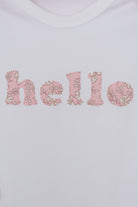 Close up of a white cotton romper with the word hello on it. the letters are cut from Capel floral liberty print and appliquéd onto the romper